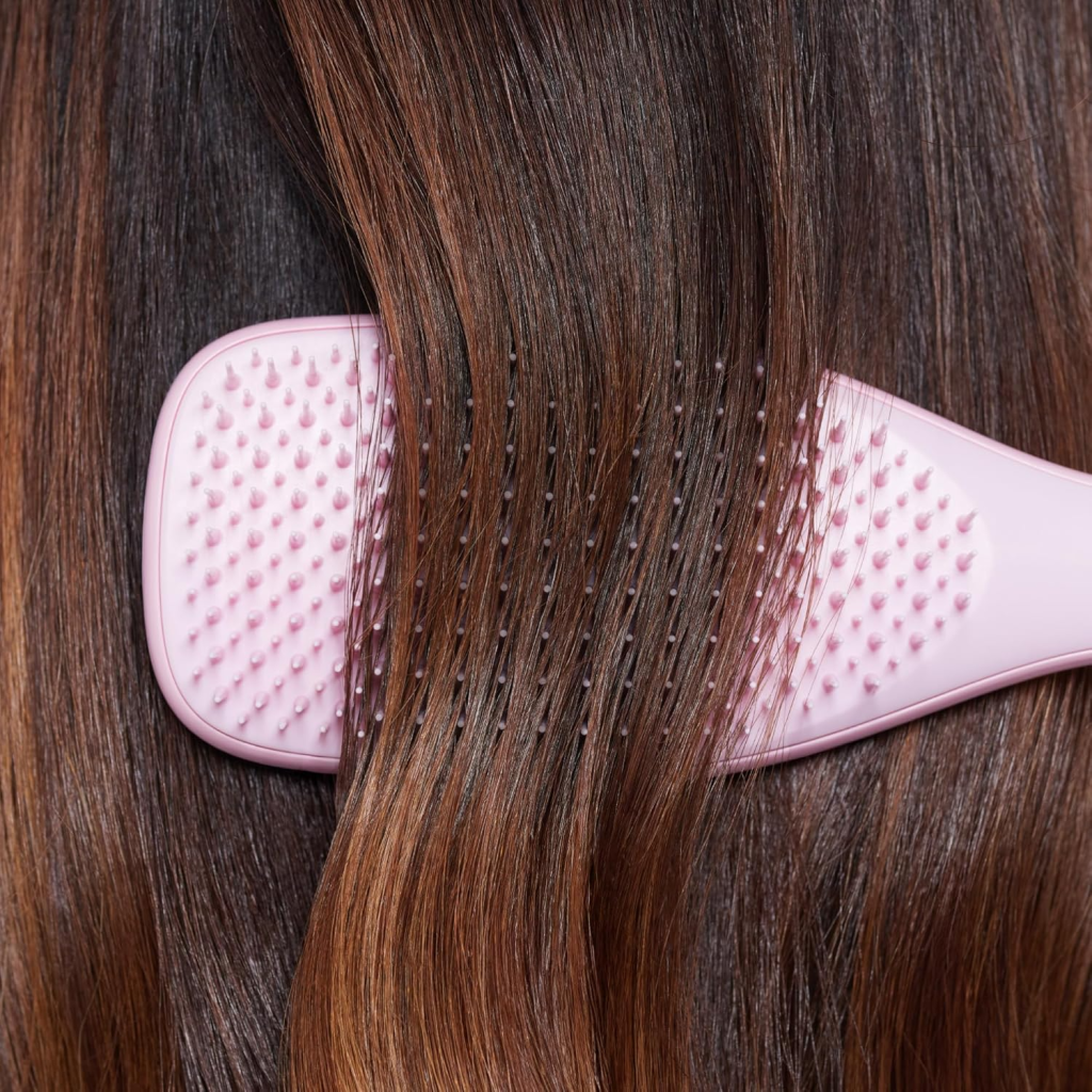 Brushing long, smooth brown hair with a pink detangler brush for silky and shiny results