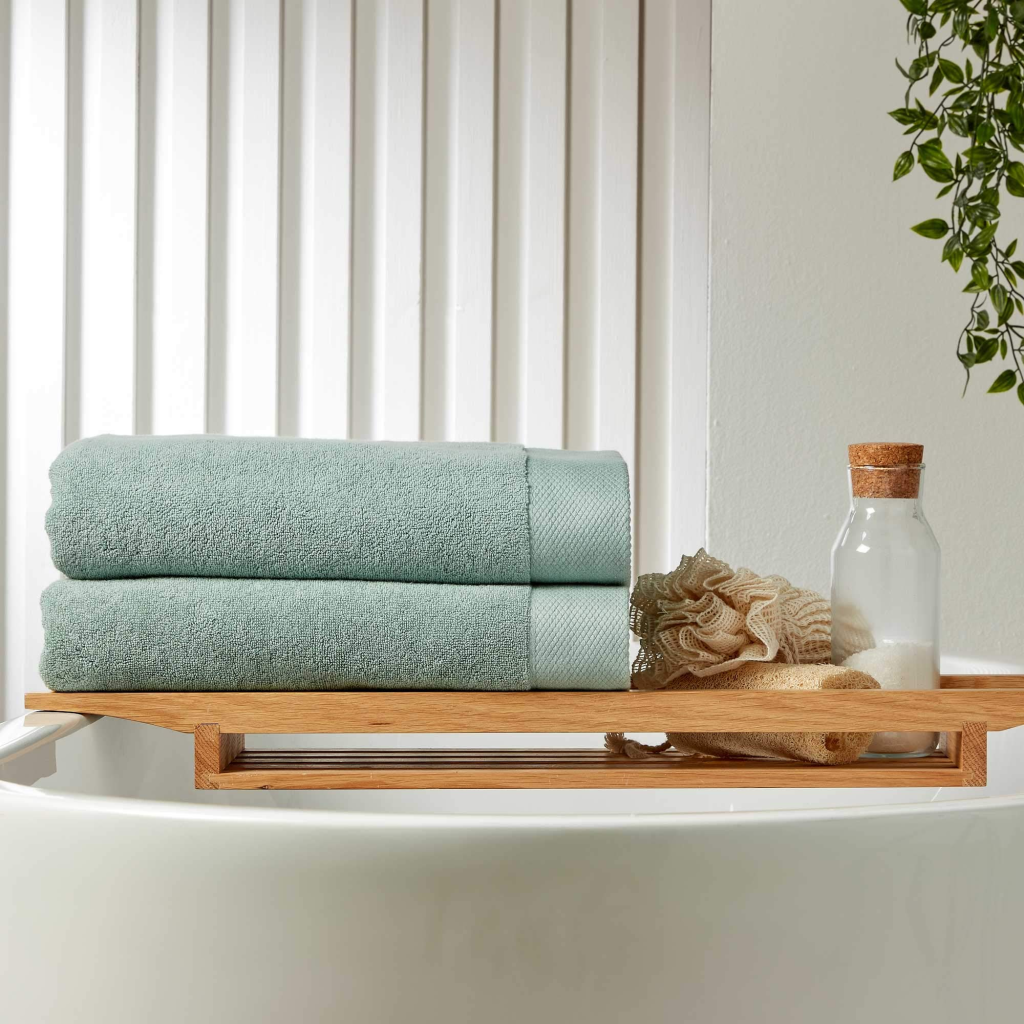 Spa-like bathroom setting with folded towels, loofah, and bath essentials on a wooden tray.