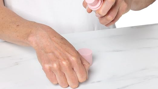 Person applying cream from a pump bottle onto their hand on a marble surface