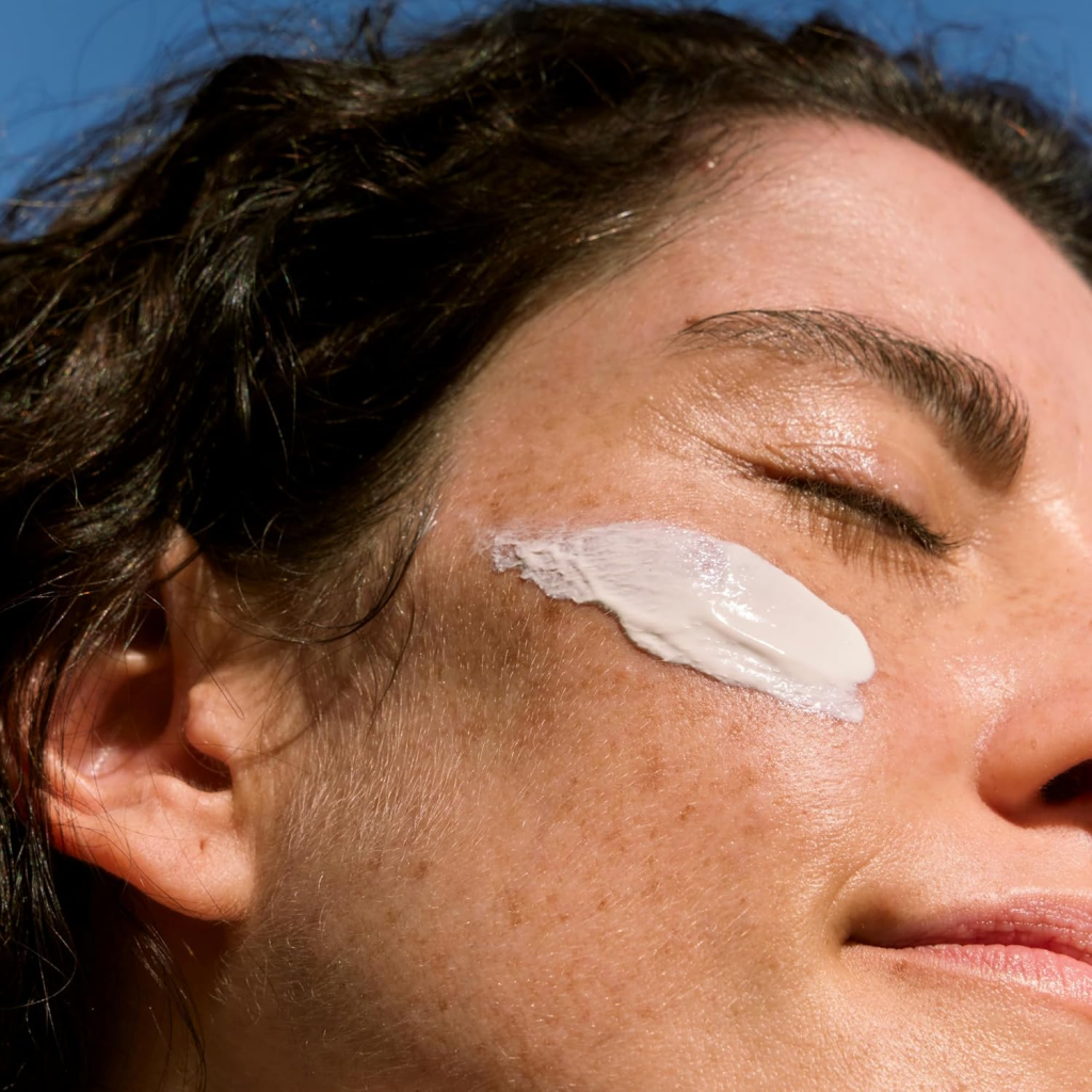 Woman applying sunscreen to her cheek, enjoying sunny weather and skin protection.