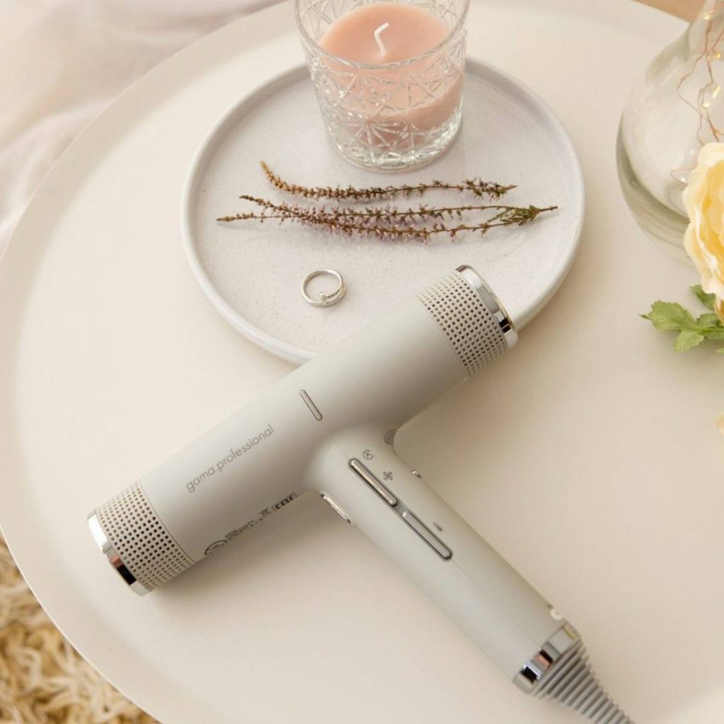Modern hairdryer on a table with a candle and a ring, creating a stylish beauty setup