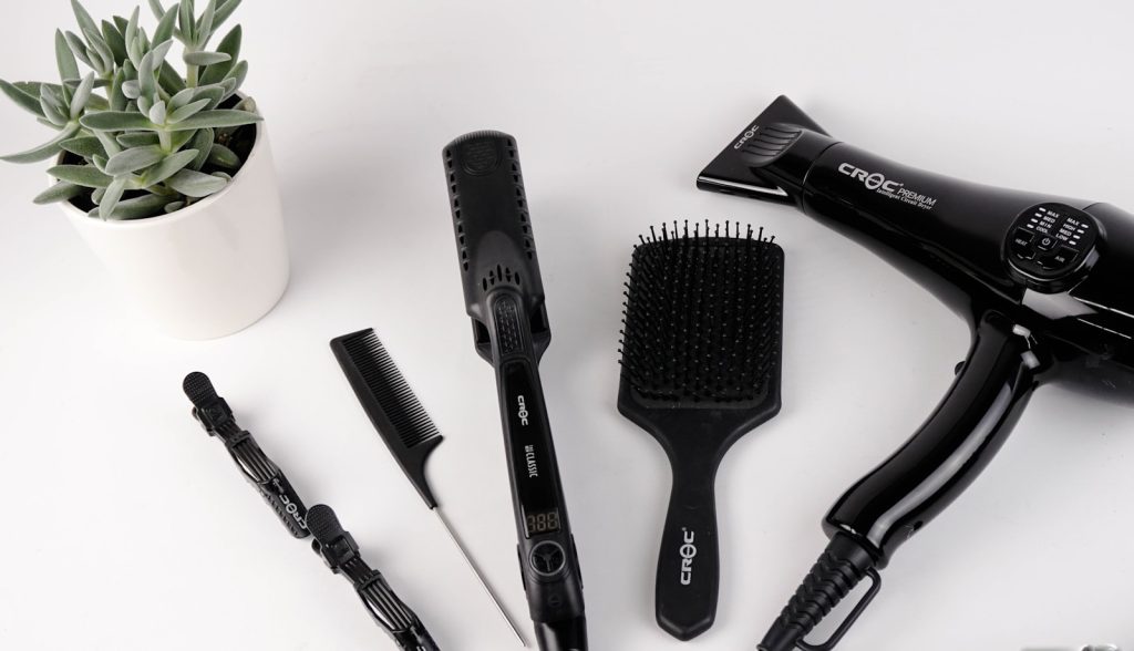 Hair styling tools and a potted plant on a white background, featuring a hairdryer, brush, comb, and clips