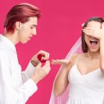 A man and woman joyfully hold up a ring, showcasing their engagement or commitment to each other