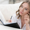 Woman thoughtfully writing in a journal while lying on a couch, reflecting with a pen in hand