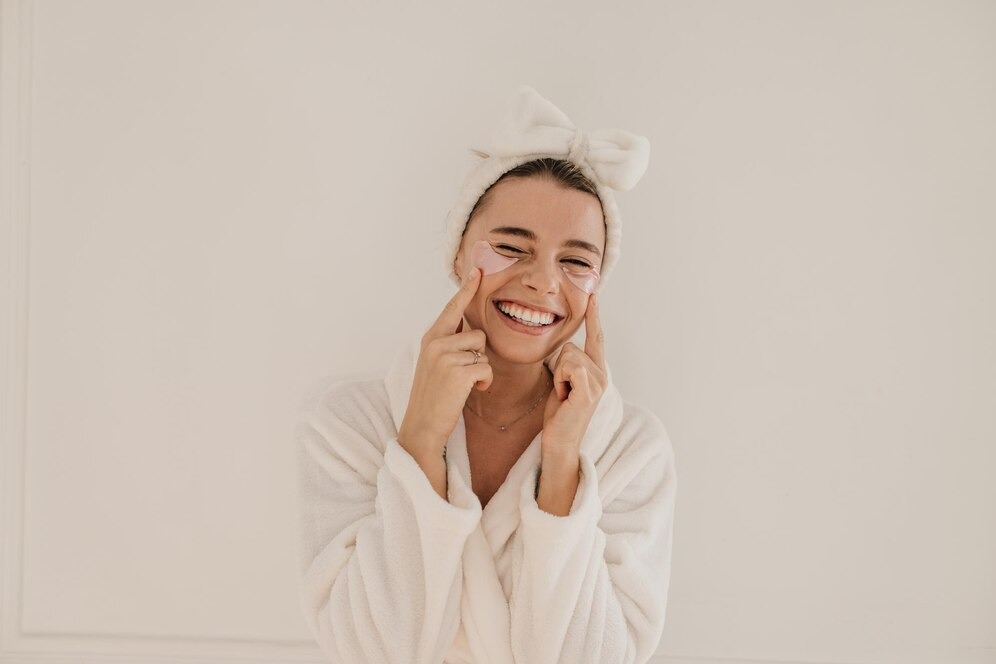 woman in a bathrobe smiles while gently holding her face, conveying a sense of joy and relaxation